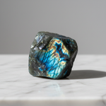 Natural Labradorite crystal with blue-gold flash on white marble – Horocosmo